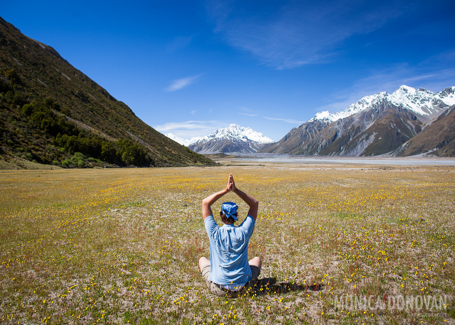 A man in a bandanna meditates in spring in front of mount cook national park, new zealand, in a field of flowers.